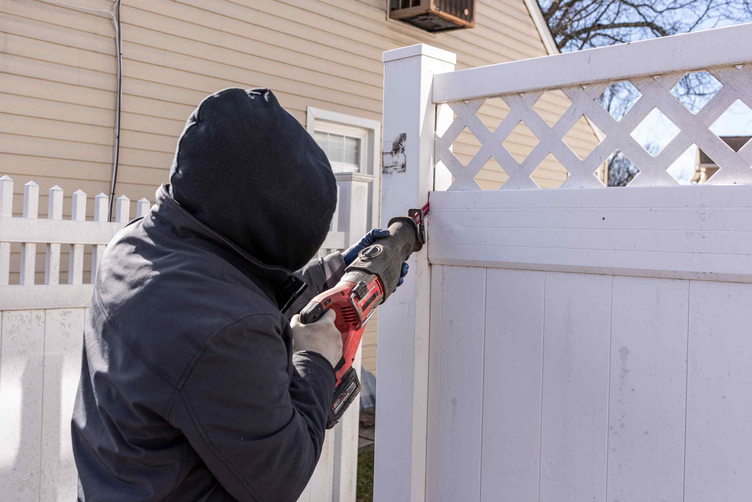 Fence Pro installer cutting a white vinyl fence panel to size with a reciprocating saw