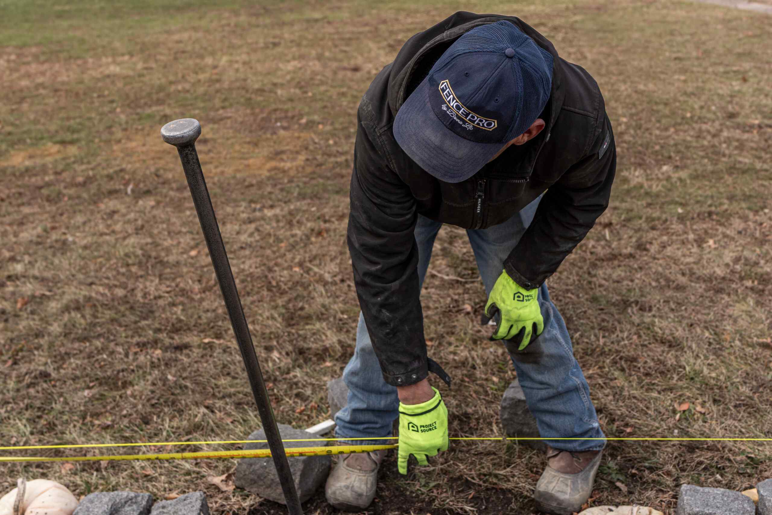 Close-up of a Fence Pro installer driving a fence post into the ground with branded work gloves